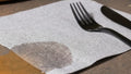A close-up image of an airlaid luncheon napkin shows it cleaning up a small spill on a wooden table, without falling apart like a standard paper napkin would.