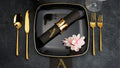A custom airlaid Naptec napkin, embossed with an "A" sits on top of a black and gold place setting