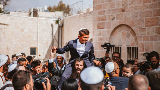 Bar Mitzvah boy lifted on shoulders during joyful celebration surrounded by guests, reflecting Naptec’s spirit of tradition and style.