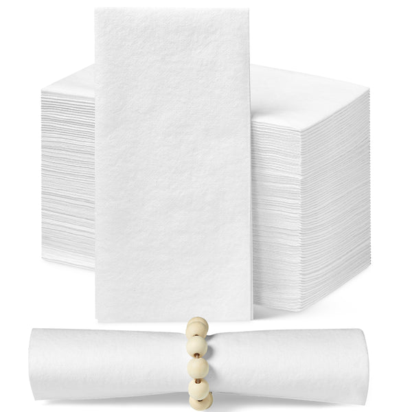 A collection of white disposable dinner napkins. A stack of white napkins is in the background. One napkin stands upright so the face of the napkin can be seen. In the foreground is a rolled up napkin in a beaded napkin ring.