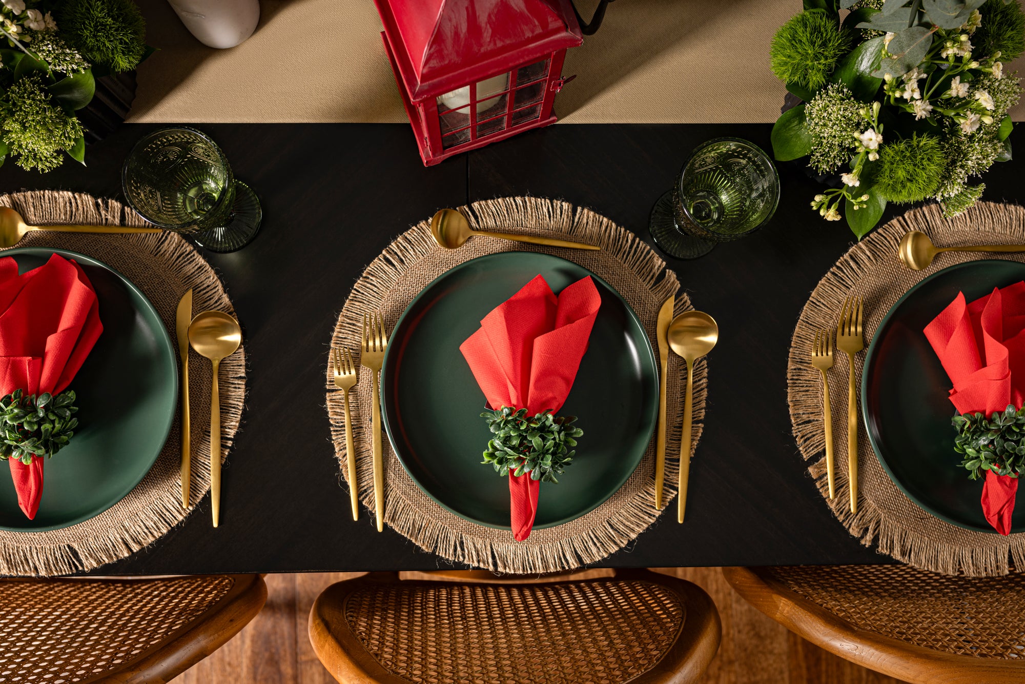 Dining table setting with green plates, red single-use disposable napkins, and gold cutlery on a black tablecloth. The image suggests a Christmas themed table setting.