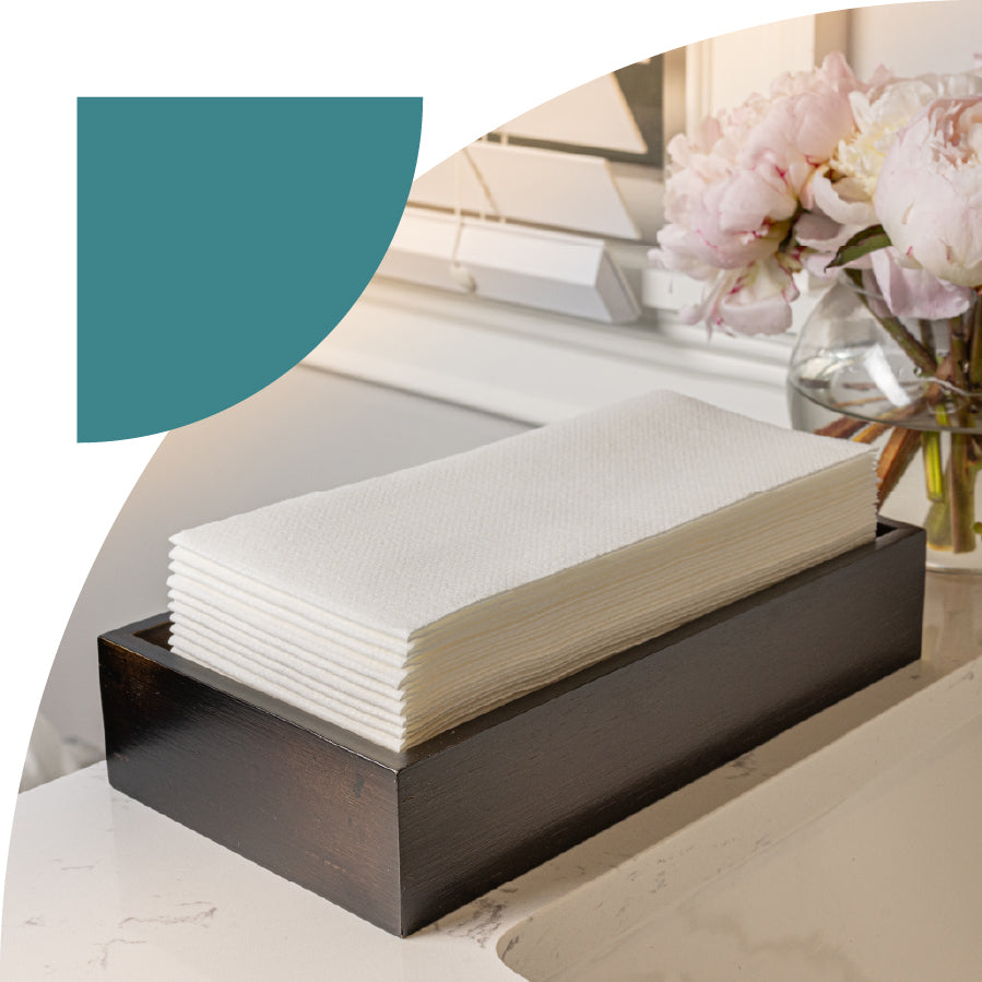 Stack of white disposable guest towels in a black holder on a marble surface with flowers in the background