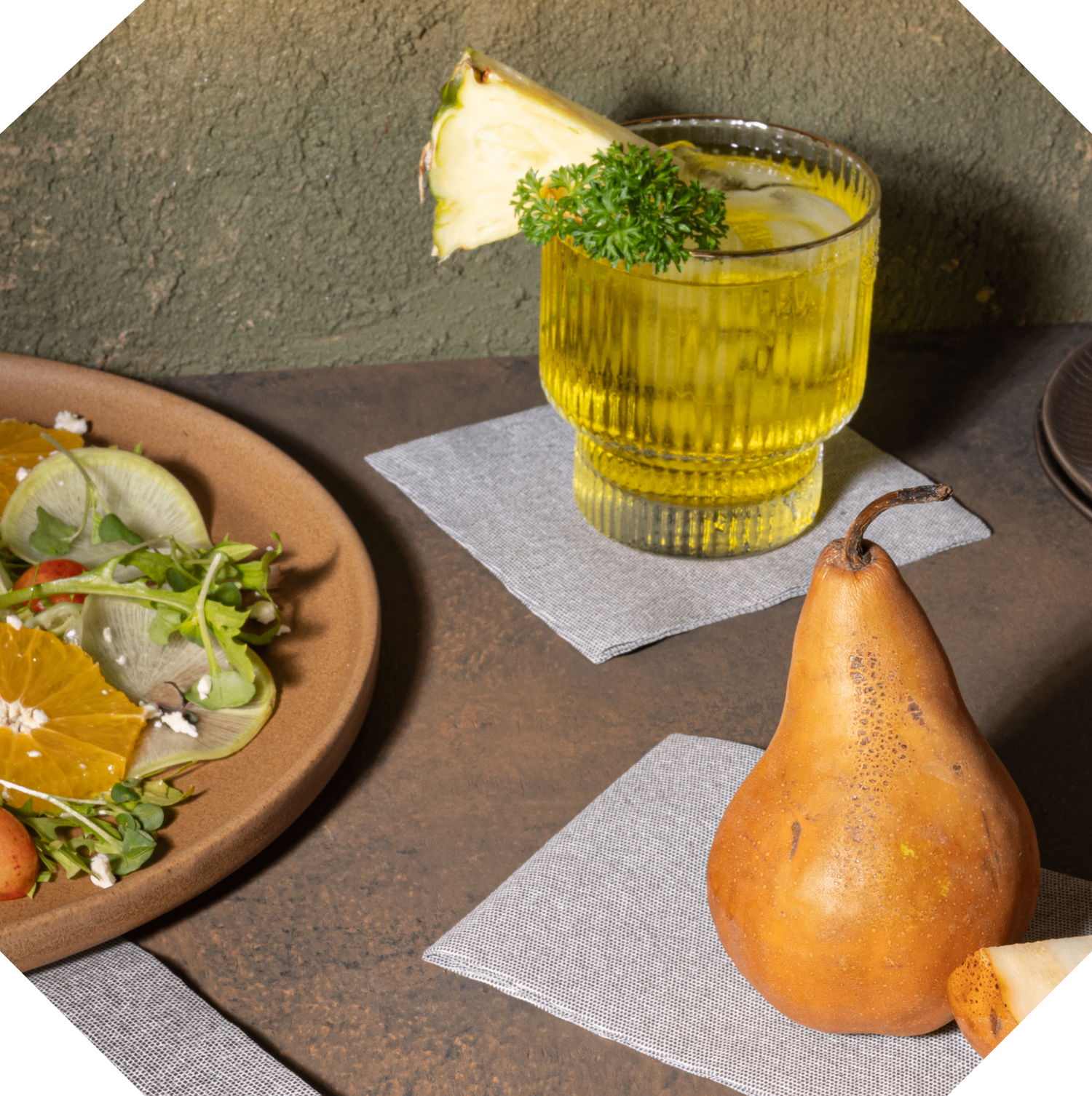 A cocktail glass with pineapple garnish sits on a Bloomingoods disposable cocktail napkin. 
