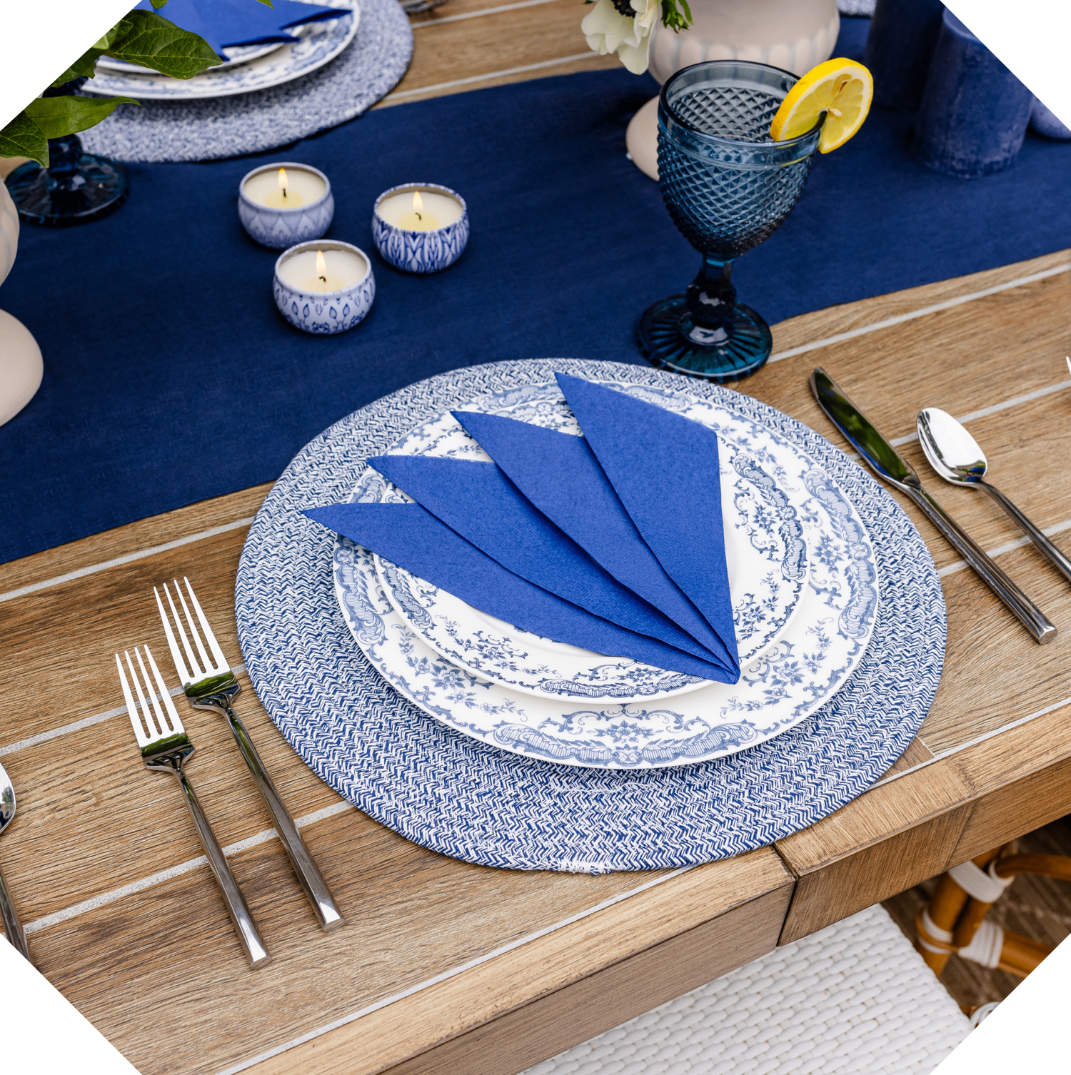 Dining table setting with blue and white napkins, plates, and cutlery on a wooden table.